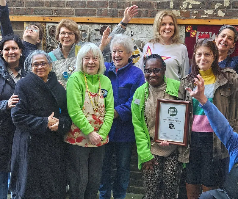 Scrapstore volunteers and staff celebrating outside the store on the Hazelhurst Estate, next to the hand-painted Scrapstore sign