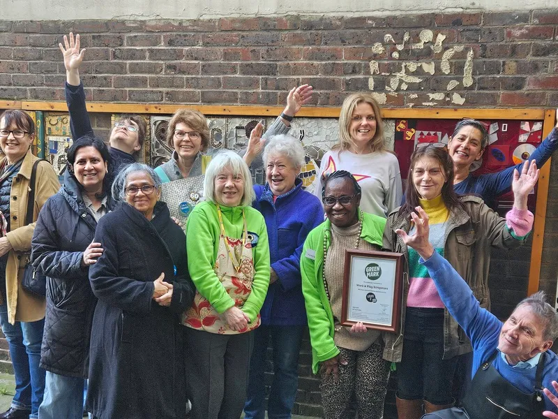 Scrapstore volunteers and staff celebrating outside the store on the Hazelhurst Estate, next to the hand-painted Scrapstore sign