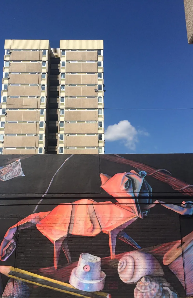 The chameleon mural by Airborne Mark beside Scrapstore, with the Hazelhurst Estate towers behind