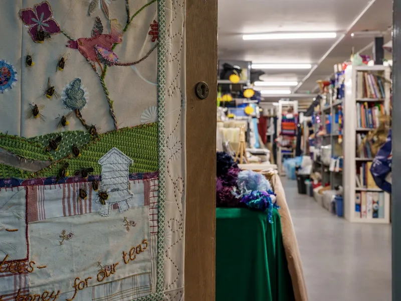 Looking through the Scrapstore door into the aisles, past a stitched bee quilt