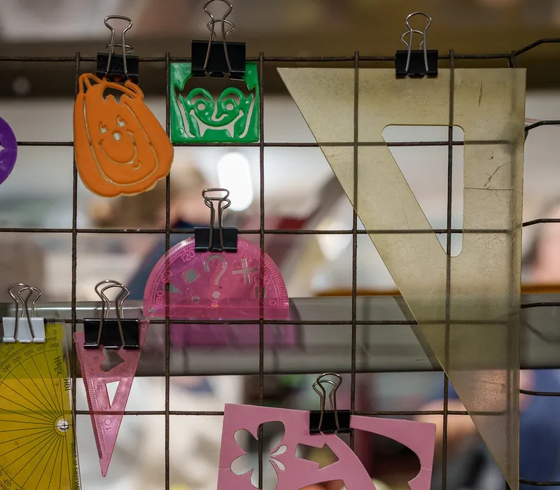 Plastic stencils in orange, green and pink, clipped to a pegboard